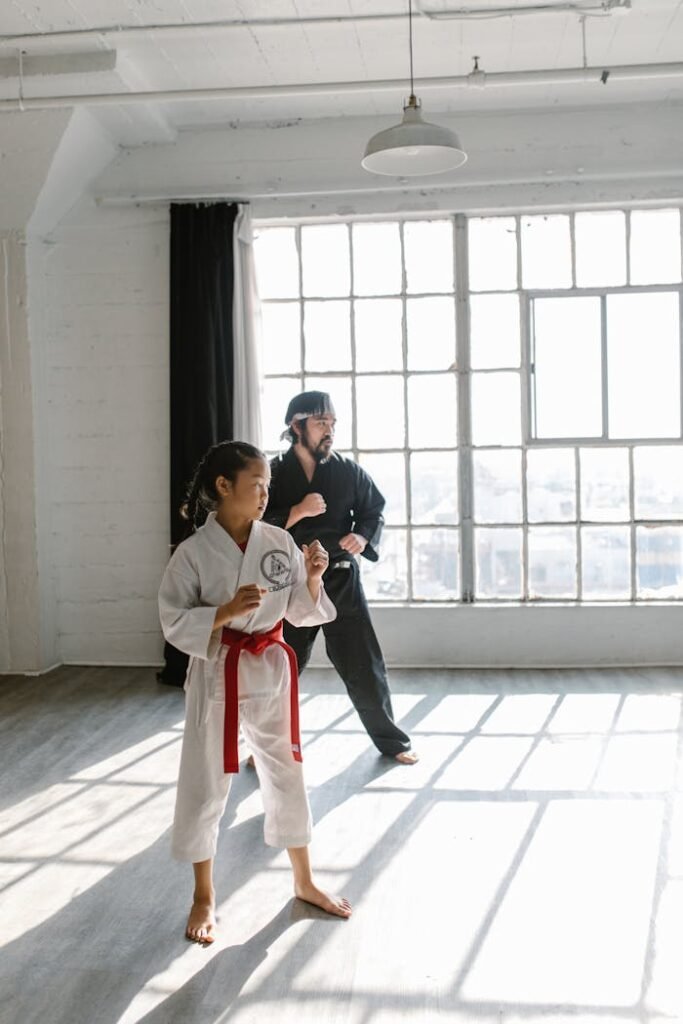 Asian girl with red belt and sensei practicing martial arts in a bright studio.